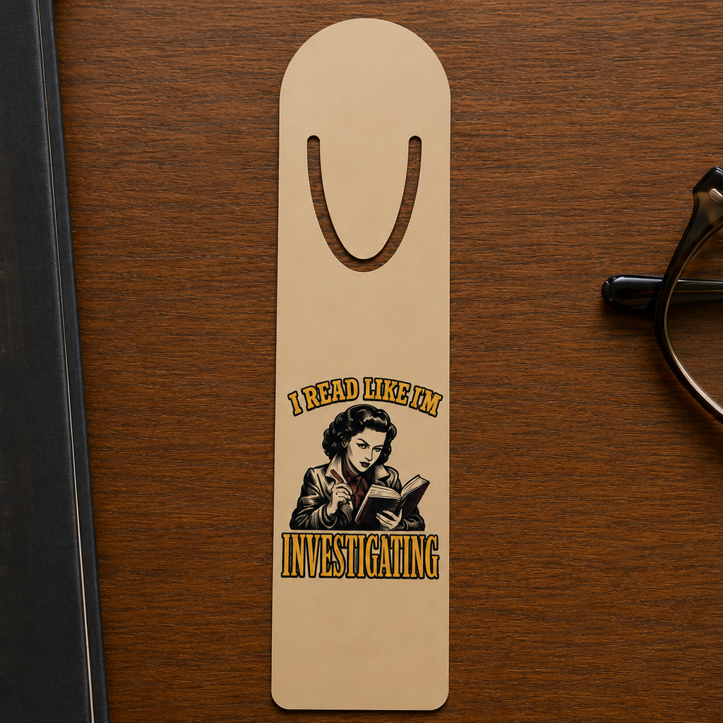 Gold-tone aluminum bookmark on a dark wood desk with an illustrated reader taking notes over an open book and the words “I Read Like I’m Investigating.”