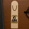 Gold-tone aluminum bookmark on a dark wood desk with an illustrated reader taking notes over an open book and the words “I Read Like I’m Investigating.”