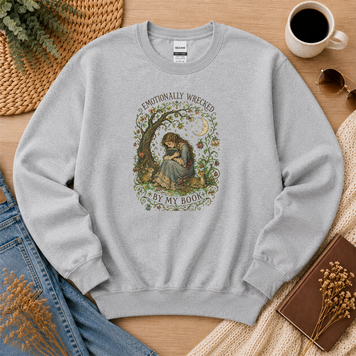 Sport gray crewneck sweatshirt laid flat with a reader beneath a tree, flowers and a crescent moon and the words “Emotionally Wrecked by My Book.”