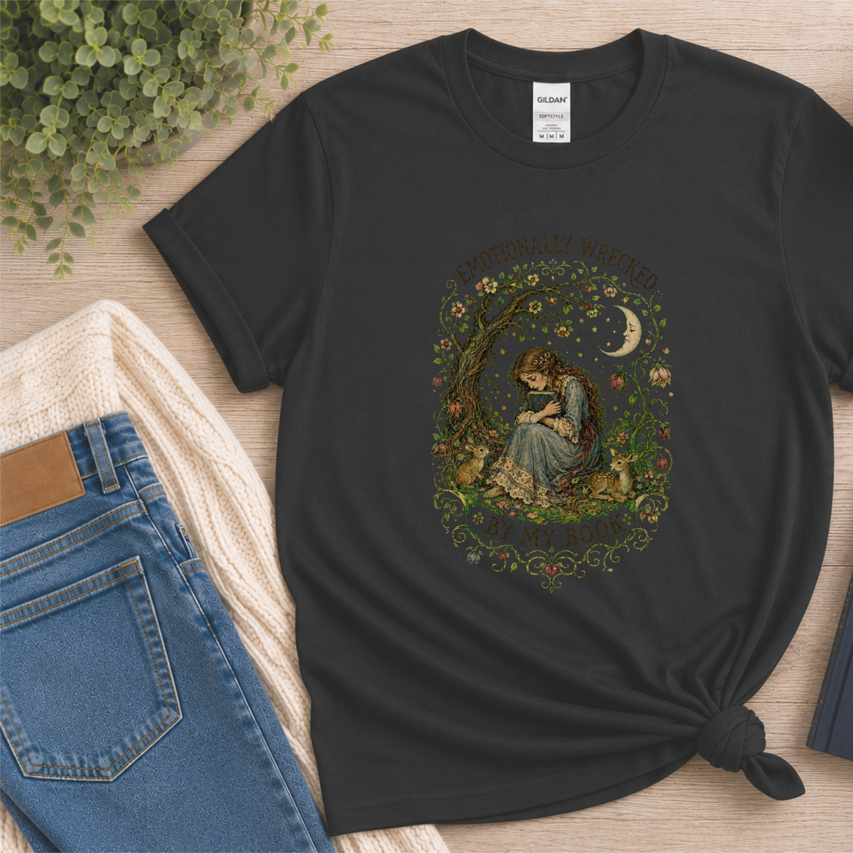 Black T-shirt laid flat with a reader beneath a tree, flowers and a crescent moon and the words “Emotionally Wrecked by My Book.”