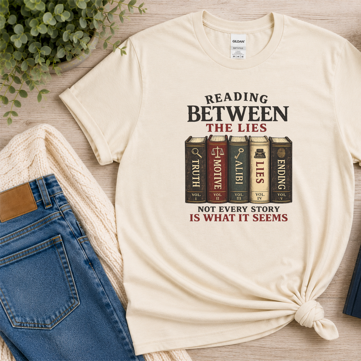 Natural cream T-shirt laid flat with books labeled Truth, Motive, Alibi, Lies and Ending and the words “Reading Between the Lies. Not Every Story Is What It Seems.”