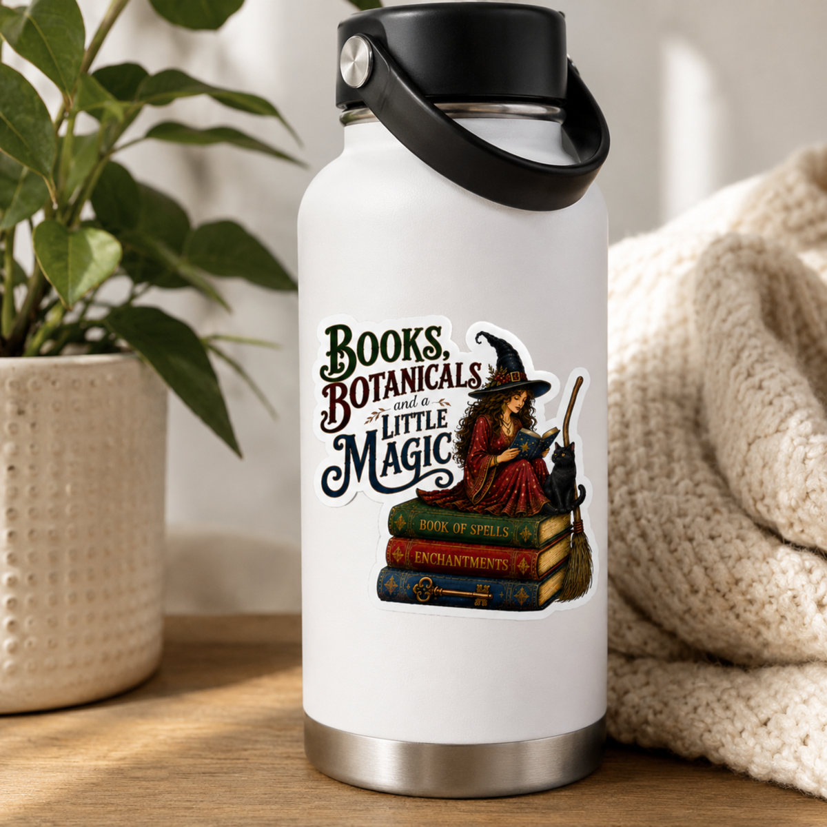“Books, Botanicals and a Little Magic” sticker with a witch in a red dress reading beside a black cat, broom, and stacked spell books, shown on a white water bottle.