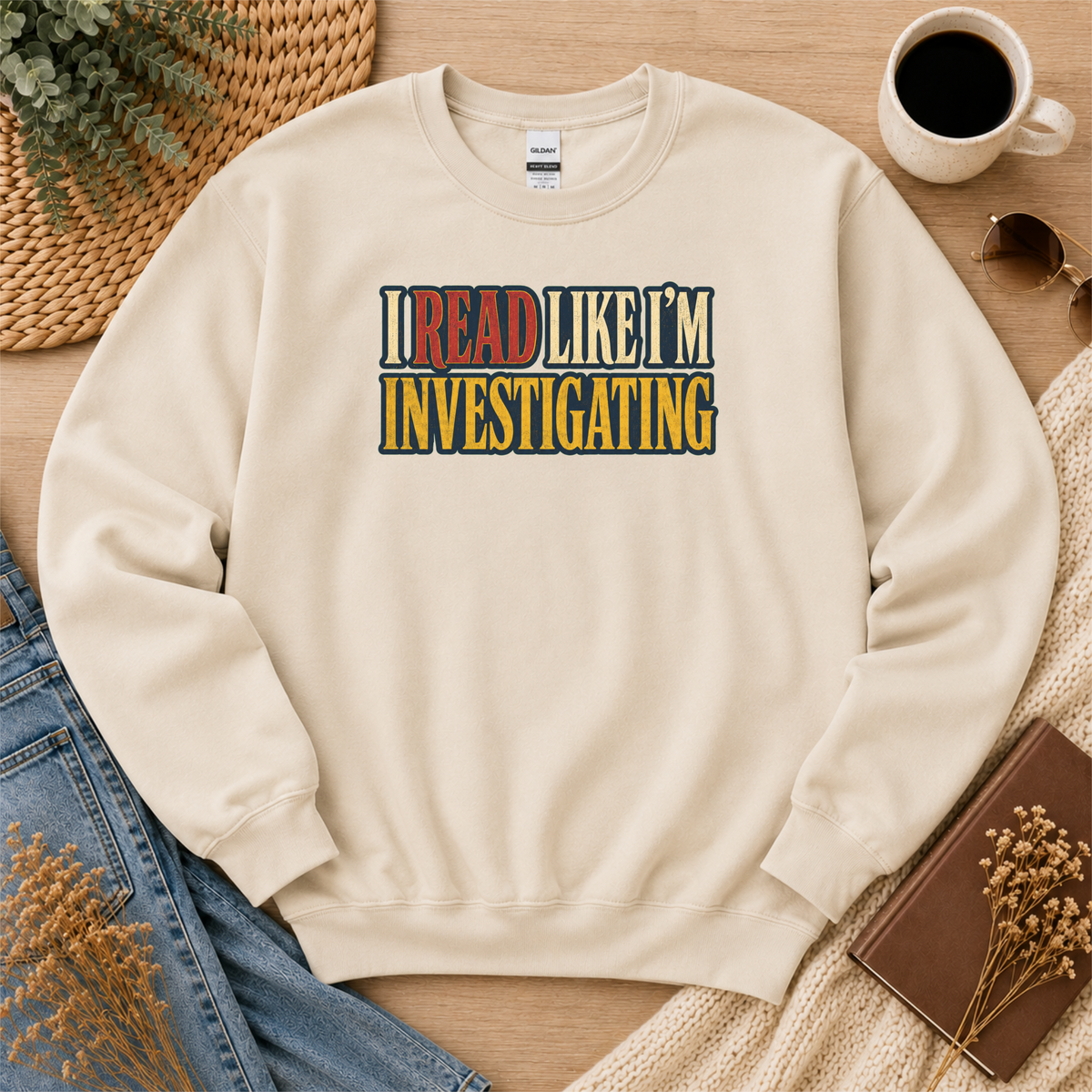 Sand crewneck sweatshirt laid flat with bold vintage lettering and the words “I Read Like I’m Investigating.”