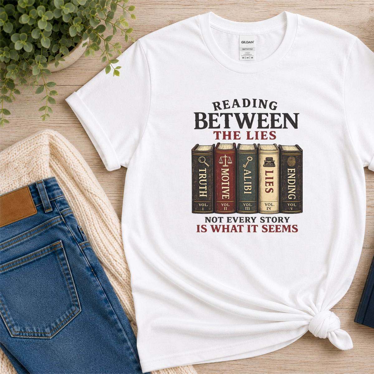 White T-shirt laid flat with books labeled Truth, Motive, Alibi, Lies and Ending and the words “Reading Between the Lies. Not Every Story Is What It Seems.”